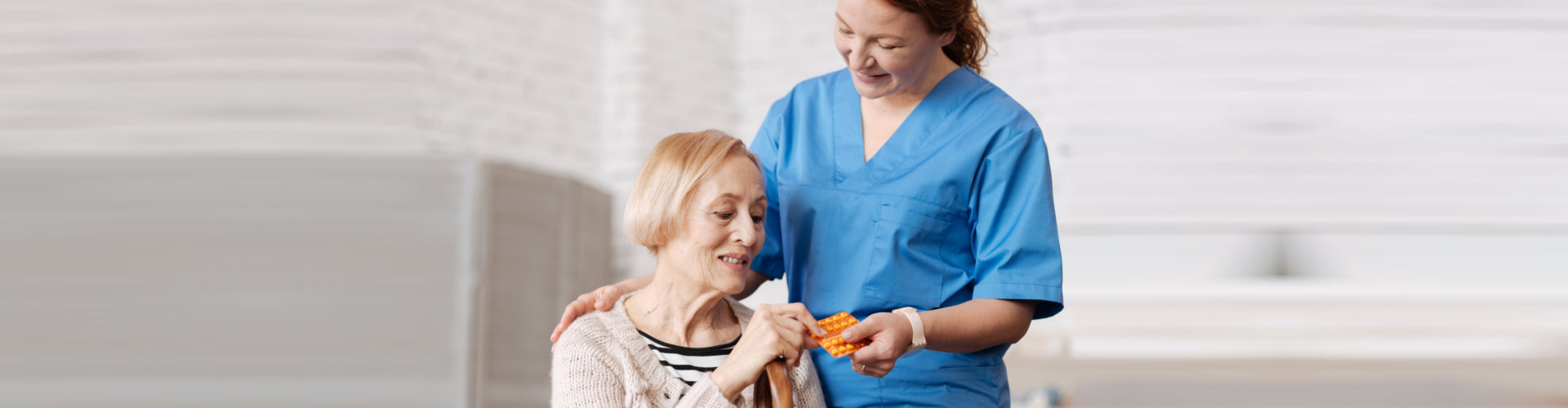 caregiver handing to senior woman a pack of pills